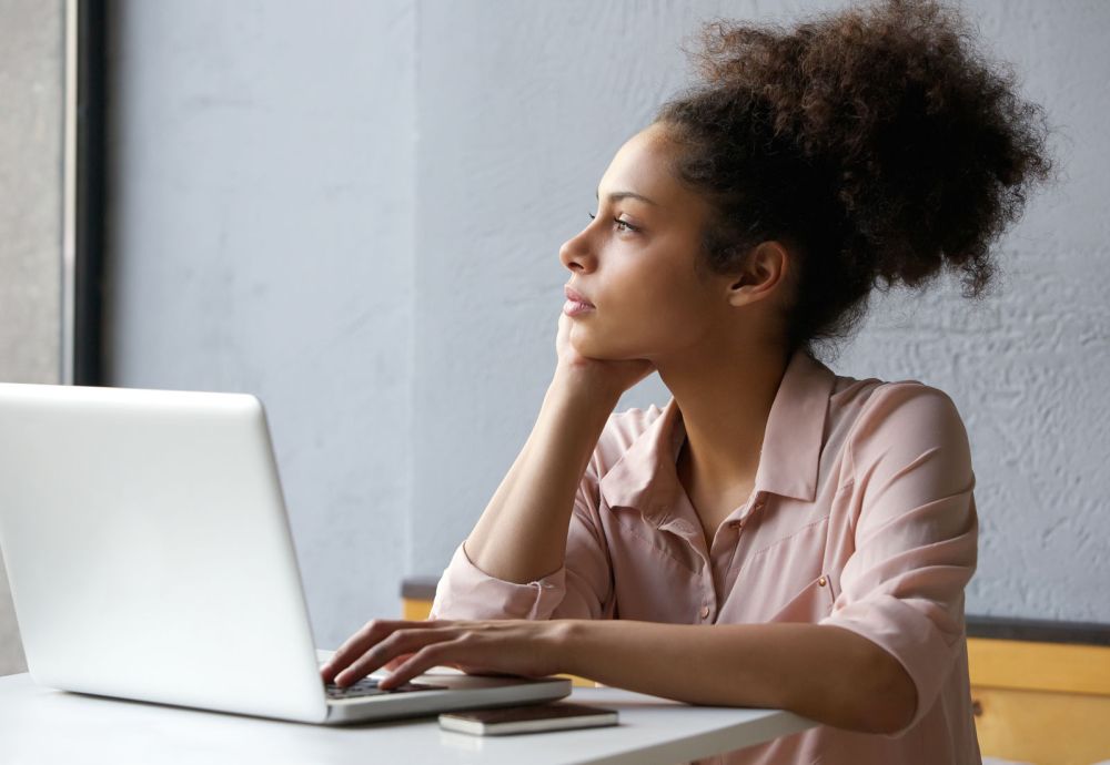 Close up portrait of a young african american woman looking out window when working on laptop